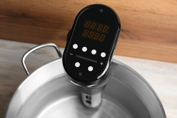 Sous vide cooker in pot on white wooden table, closeup. Thermal immersion circulator
