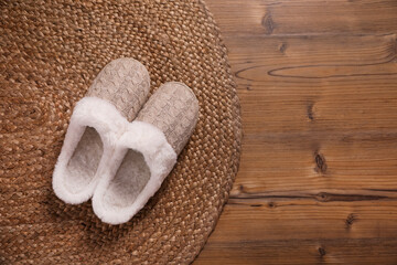 Fototapeta na wymiar Pair of warm stylish slippers and wicker mat on wooden floor, flat lay. Space for text