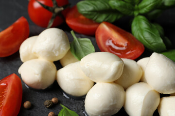 Delicious mozzarella balls, tomatoes and basil leaves on black table, closeup