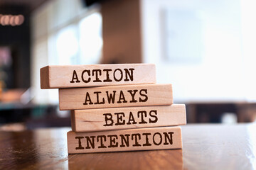 Wooden blocks with words 'Action Always Beats Intention'.