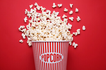 Overturned paper bucket with delicious popcorn on red background, flat lay