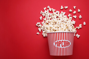 Overturned paper bucket with delicious popcorn on red background, flat lay. Space for text © New Africa