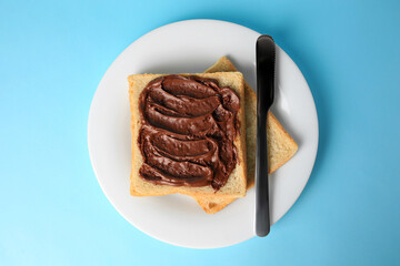 Tasty toast with chocolate paste on light blue background, top view