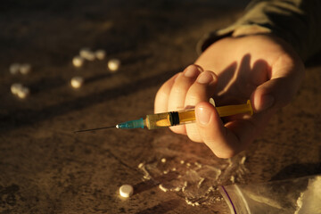 Addicted man with syringe near drugs at grey textured table, closeup. Space for text