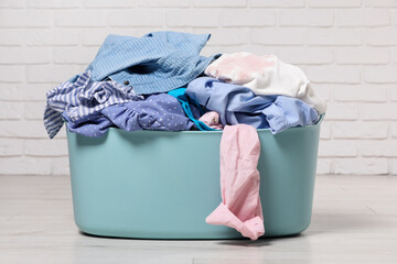 Laundry basket with clothes near white brick wall