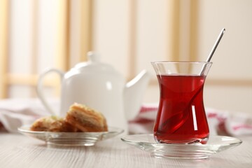 Glass of traditional Turkish tea and sweet baklava on white wooden table indoors. Space for text