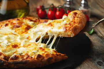 A slice of hot Italian pizza with stretching cheese. Pizza four cheeses with basil.