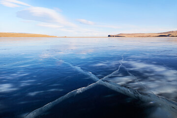 Frozen Lake Baikal on a sunny winter day. Beautiful pattern with cracks of transparent smooth ice....