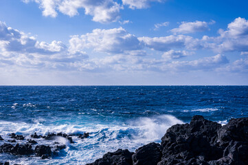 八丈島の青い海の水平線に浮かぶ白い雲と黒い岩