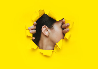 Fototapeta Female ear and two hands close-up. Copy space, torn paper and yellow background. The concept of eavesdropping, espionage, gossip and the yellow press. obraz