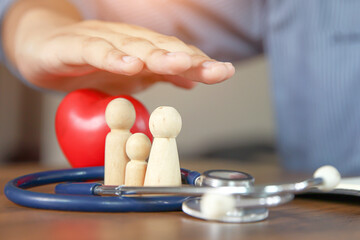 Doctor hand protect wooden doll with heart and stethoscope concept of health care safety family insurance or health checkup or healthy planning or sick prevention.