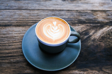 Blue ceramic cup of cappuccino on wooden background with beautiful latte art