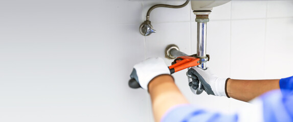 Technician plumber using a wrench to repair a water pipe under the sink. Concept of maintenance,...