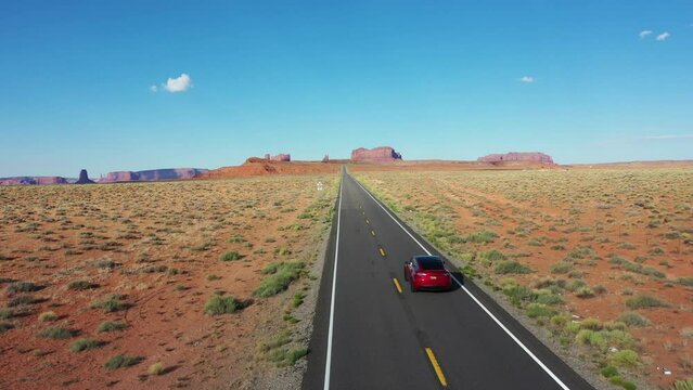 Drone shot of a car driving on State Route 163 in Utah toward Monument Valley on a sunny day on America road trip.
