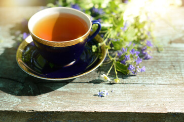 Summer tea, cup of herbal tea and bouquet strawberry flowers and blue wildflowers on wooden table in garden outdoor, blurred background, soft focus, copy space
