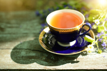 Cup of tea and wildflowers bouquet on a wooden table outdoor. Herbal Tea, wildflowers and herbs on a blurred background, soft focus