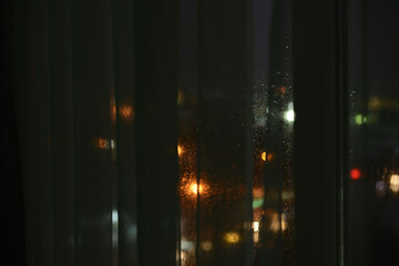 raindrops on the window at night, view through transparent window curtains, blurred abstract...