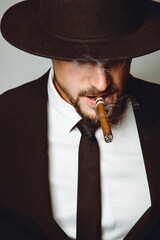 Portrait of a young and handsome model in a classic black and white style clothing in a hat witha cigar. Studio shot. Copy space.