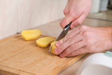 A man cuts potatoes in half with a knife to use food processor. Preparation of potatoes for cooking. A man cooks dinner or lunch at home for the family.