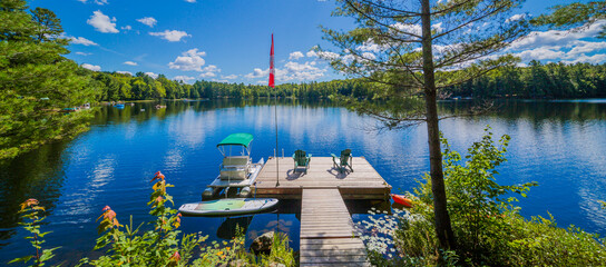 Two Ontario chairs sitting on a wood dock facing a calm lake. - obrazy, fototapety, plakaty