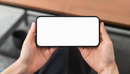 Hands holding smartphone with mockup of blank screen on sofa in living room.