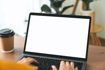 Hand using laptop and typing on keyboard with mockup of blank screen on wooden table.