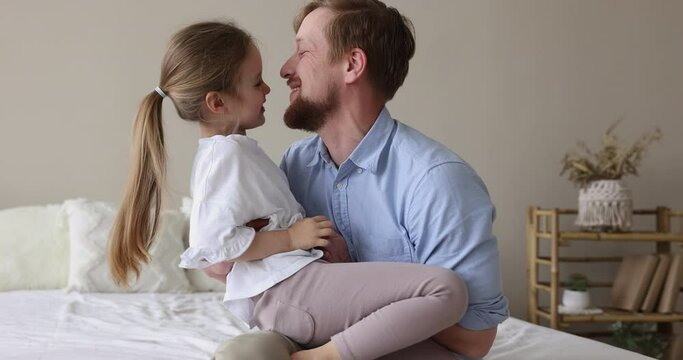 Pretty little girl enjoy funny playtime with loving father seated on his laps, play together in cozy bedroom, relish leisure and communication feel happy. Fatherhood, unconditional love, family ties
