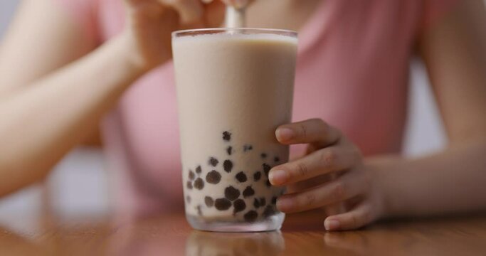 Popular Taiwan drink - a woman use a glass straw drinking Bubble milk tea in drinking glass on table close up