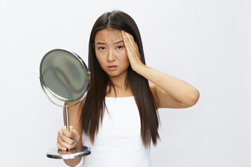 Asian woman with mirror in hand facial skin problems, acne and inflammation, red rash and...
