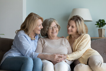 Senior mom and young adult daughter visiting elder senior grandmother, resting on sofa at home,...