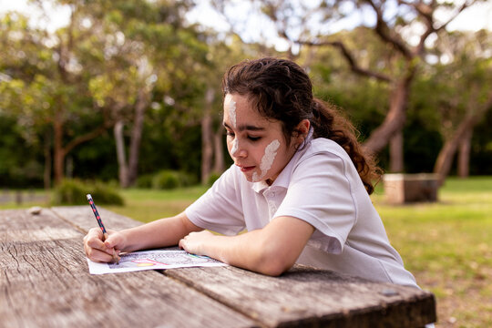 Young Aboriginal girl with face paint drawing at a table outdoors