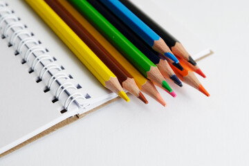 colored pencils against the background of a desk, notebook, white wall