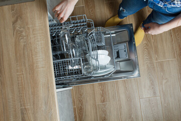 The girl takes out clean glasses from the dishwasher. clean dishes in the dishwasher. modern...