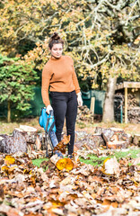 Young woman with her electric blower making piles of dead leaves to clean up the garden