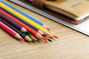 Obraz premium colored pencils against the background of a desk, notebook, white wall
