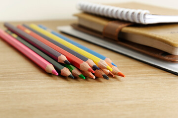 Naklejka premium colored pencils against the background of a desk, notebook, white wall