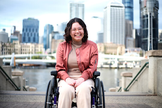 Smiling woman with a disability sitting in a wheel chair with tall buildings behind her