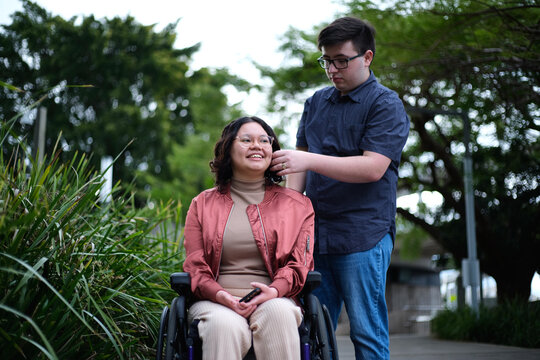 Portrait of man standing and a woman with a disability in a wheel chair outside