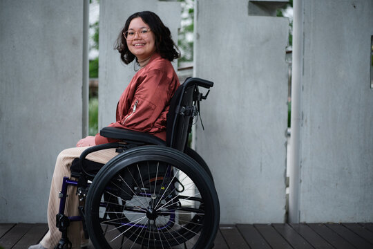 Smiling woman with a disability sitting in a wheelchair outside in urban setting