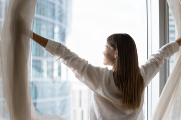 Luxury apartment owner or female traveler opens curtains, welcoming new day, standing near...