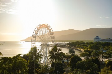 Golden hour over the ferris wheel, treetops, lagoon and hilly backdrop of Cairns Esplanade - Coral Sea, Cairns; Far North Queensland, Australia - obrazy, fototapety, plakaty