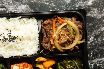 Beef bulgogi and various side dishes in a packaging container