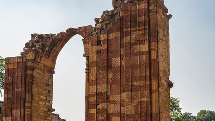 Ruins of the ancient temple complex Qutab Minar. The dilapidated arch of red sandstone against the...