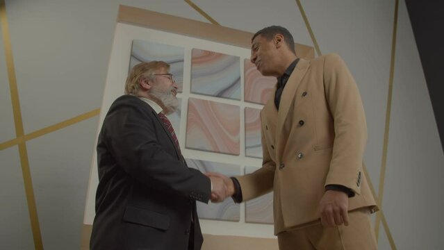 Professional successful positive diverse multiracial businessmen in suits handshaking at office, showing friendliness, readiness for mutually beneficial cooperation while meeting at office.