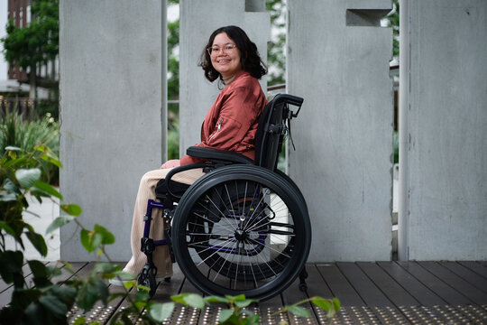 Smiling woman with a disability sitting in a wheelchair outside in urban setting with greenery