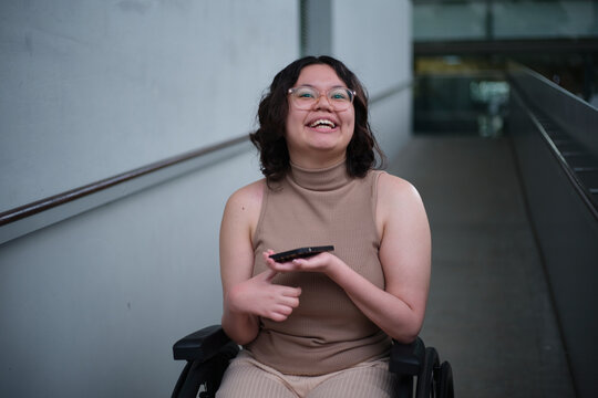 Smiling woman with a disability sitting in a wheelchair indoors holding a mobile phone
