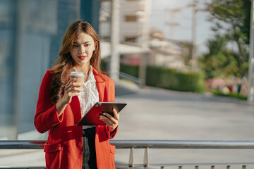 Asian women using digital tablet computer and holding coffee to go while working at office.