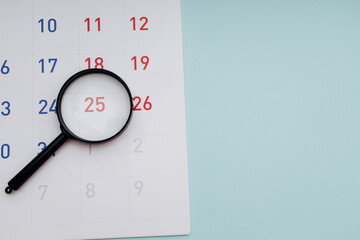 Black magnifying glass and calendar on blue background close-up