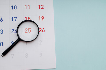 Naklejka premium Black magnifying glass and calendar on blue background close-up