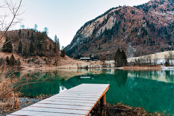 A mountain lake landscape in the Alps with turquoise water with a wooden pier and reflections on the water surface